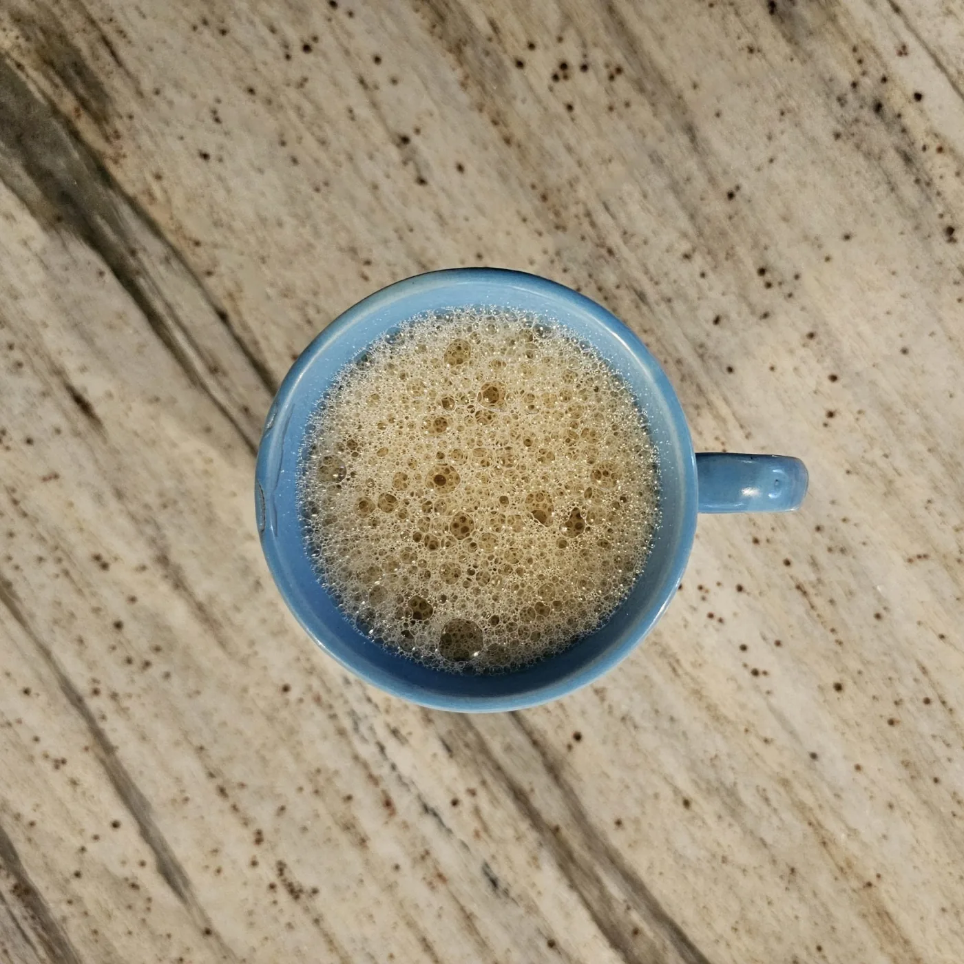 Top view of a blue cup of frothy tea on a light wooden table with dark grain