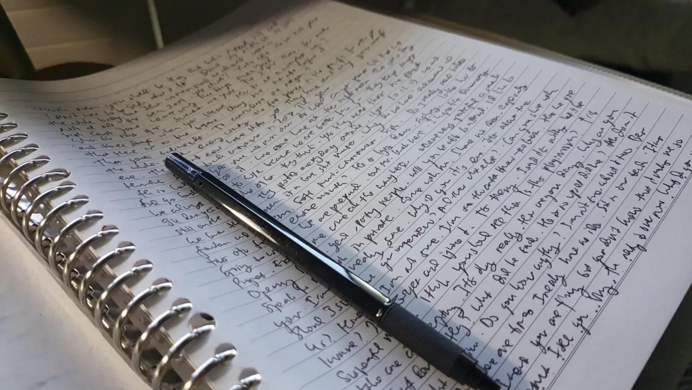 Black pen resting on an open spiral notebook filled with handwriting