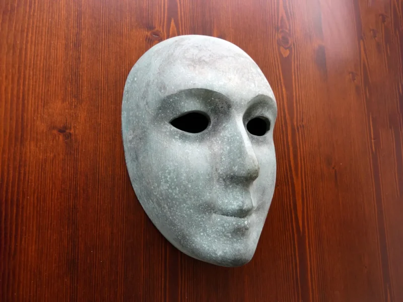 Smooth white mask of a calm, expressionless face mounted on a dark red wooden board