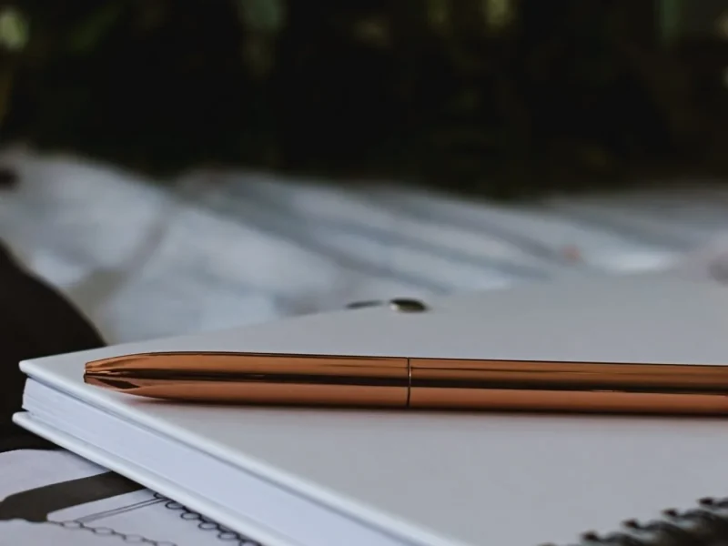 Copper pen lying on a closed white spiral notebook
