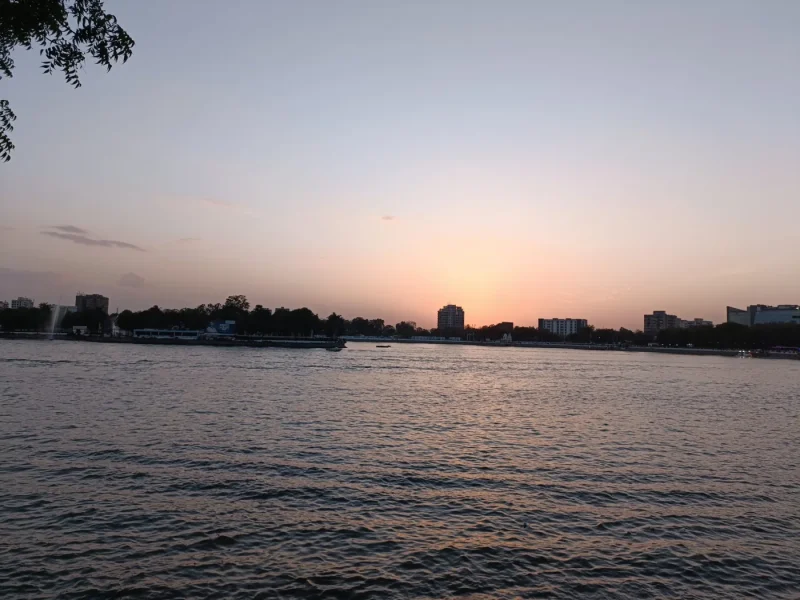 Calm water at sunset with a pink and grey sky and a low city skyline along the far shore